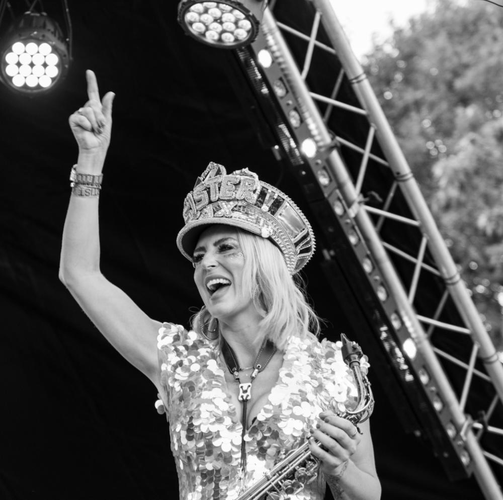 Black and white photo of Kay laughing, arm in the air on stage at a festival.