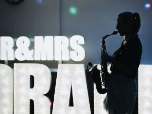 Silhouette of Kay playing sax infront of larger letter lights